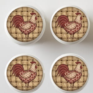 May include: Four white cabinet knobs with a rooster design. Each knob features a rooster illustration with a red comb, tail, and heart-shaped accents on a woven background. The rooster is set against a light brown woven pattern.