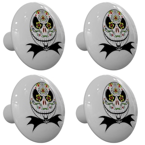 May include: Set of four white ceramic cabinet knobs with a black and white image of a skull with a sugar skull design. The skull has a toothy grin and is decorated with colorful flowers and swirls.