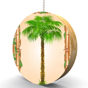 May include: A round, wooden ceiling fan pull with a tropical palm tree design. The palm tree has green leaves and a brown trunk. The background is a light orange color with a bamboo pattern.