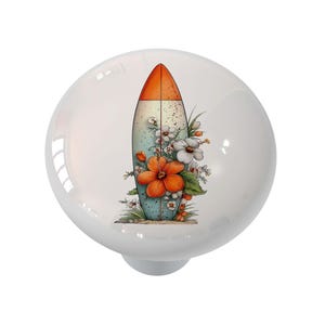 May include: White ceramic cabinet knob featuring a surfboard design. The surfboard is decorated with orange and blue colors, and adorned with orange and white flowers. A decorative accent for furniture.