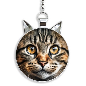 May include: A silver ceiling fan pull chain with a round, silver-rimmed pendant featuring a close-up image of a tabby cat's face. The cat has large, golden eyes and a brown nose.