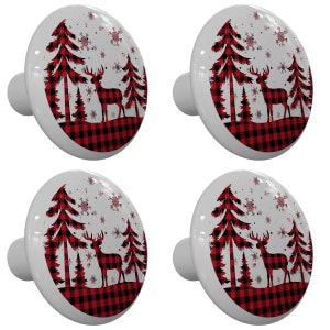 May include: Set of four ceramic cabinet knobs featuring a red and black buffalo plaid pattern with a silhouette of a deer and pine trees against a white background with snowflakes.