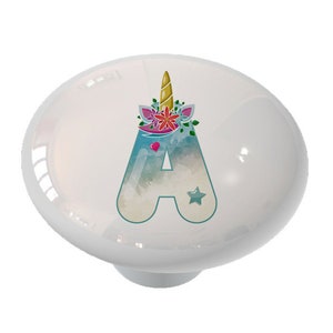 May include: White ceramic knob with a watercolor-style letter A, decorated with a unicorn horn and flowers. The letter is in a teal blue color with a pink heart and a gold star.