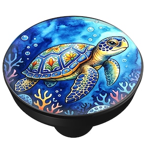 May include: A round cabinet knob featuring a vibrant watercolor illustration of a sea turtle swimming underwater. The turtle has a patterned shell with orange and yellow floral accents, set against a deep blue background with coral and bubbles.