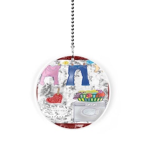 May include: A white round fan pull with a red, white, and blue laundry room design. The design features a clothesline with clothes hanging on it, a washing machine, and a basket of laundry. The text "Laundry Room" is written in a red, white, and blue font. The text "Wash, Dry, Fold, Repeat" is written in a smaller font below the main text.