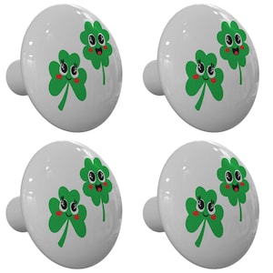 May include: Four white ceramic cabinet knobs with a green shamrock design. Each knob features two shamrocks with smiling faces. The shamrocks have red cheeks and black eyes.