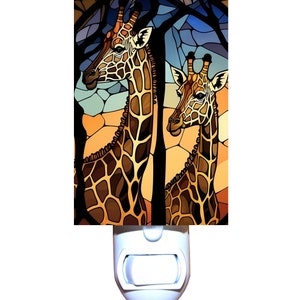 May include: A decorative night light featuring a stained-glass style image of two giraffes. The giraffes have brown and tan patterned coats, set against a backdrop of orange, blue, and black. The night light has a white plastic base.