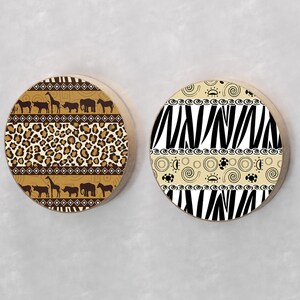 May include: Two round wooden wall decor pieces with different African-inspired patterns. One features a brown and black leopard print with a black and white geometric pattern. The other features a black and white zebra stripe pattern with a brown and white geometric pattern.