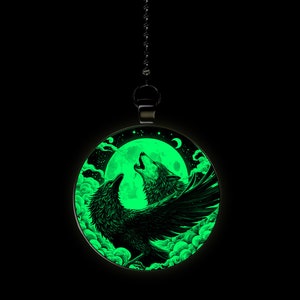 May include: A round, black pendant with a glow-in-the-dark design of a wolf and a raven howling at the moon. The moon is full and green, and the sky is filled with clouds.