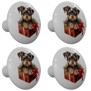 May include: Four white ceramic cabinet knobs. Each knob features a Yorkshire Terrier puppy inside a red and gold gift box with a red bow. The puppy has brown and black fur and is surrounded by green foliage.