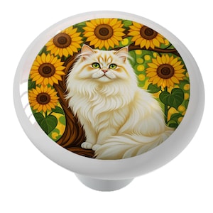 May include: White cabinet knob with a decorative design featuring a fluffy white cat with yellow accents, set against a backdrop of sunflowers and green foliage. The knob has a glossy finish and a rounded shape, suitable for furniture or decor.