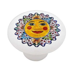 May include: A white ceramic knob with a colorful sun face design. The sun has a yellow face with blue eyes, red cheeks, and a red smile. The sun is surrounded by a blue and white floral pattern.