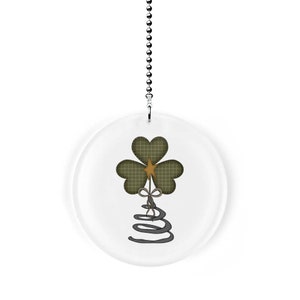 May include: A round, clear acrylic fan pull with a green shamrock design and a gold star. The shamrock has a plaid pattern and a brown bow. The fan pull is attached to a silver chain.