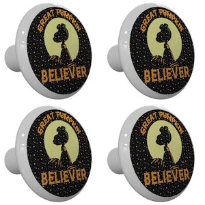 May include: Set of four white ceramic cabinet knobs with a black and yellow design. The design features a silhouette of the Great Pumpkin from the Peanuts cartoon with the text "Great Pumpkin Believer".