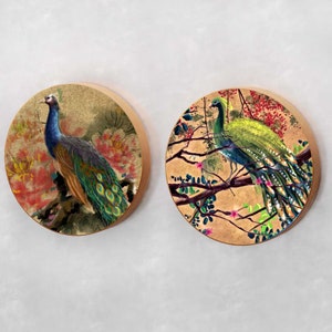 May include: Two round wall decor pieces with a gold background and a peacock design. One peacock is blue and green, the other is green and yellow. Both peacocks are surrounded by flowers and branches.