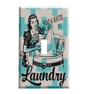 May include: A light switch cover with a vintage illustration of a woman doing laundry. The illustration is in black and white and features a woman in a dress and apron, putting clothes into a washing machine. The background is a light blue and white checkered pattern. The text "SOAP & WATER 5¢" is above the illustration, and the text "Laundry" is below the illustration.