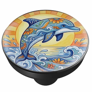May include: A round knob featuring a colorful illustration of a dolphin leaping from ocean waves. The dolphin is decorated with blue and orange floral patterns. The background shows a bright yellow and orange sun setting over the water.