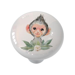 May include: White ceramic cabinet knob featuring a watercolor illustration of a monkey with gray fur, pink ears, and a floral accent. The knob has a glossy finish and a round shape, suitable for furniture.