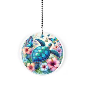 May include: A round, white ceiling fan pull featuring a vibrant illustration of a sea turtle surrounded by colorful butterflies and hibiscus flowers. The turtle has a blue and green shell. The butterflies have blue, yellow, and orange wings.