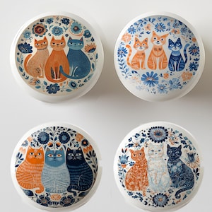 May include: Four white ceramic decorative plates with cat illustrations. Each plate features a different arrangement of cats in shades of orange, blue, and black, surrounded by floral patterns in blue and white. The plates are round and have a glossy finish.