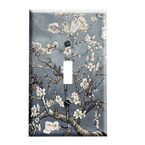 May include: A decorative light switch cover featuring a painting of a blossoming tree branch with white flowers against a gray background. The artwork includes brown branches and a white switch opening.
