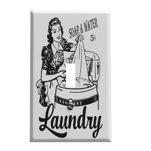May include: A black and white illustration of a woman doing laundry. The illustration is on a white light switch cover with the text "SOAP & WATER 5¢ Laundry".