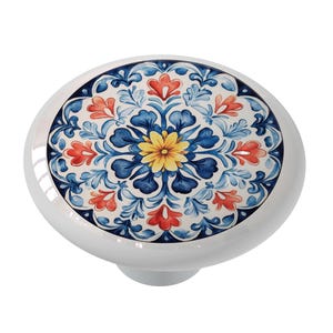 May include: A white ceramic knob with a blue, red, and yellow floral design. The knob has a round base and a raised center.