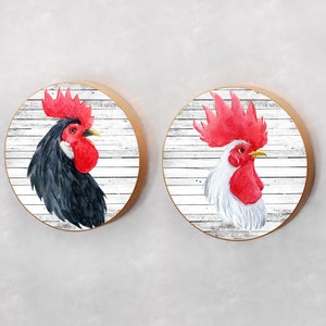 May include: Two round wooden signs with a whitewashed wood background and a watercolor rooster illustration. One rooster is black and white, the other is white with a red comb and wattle.