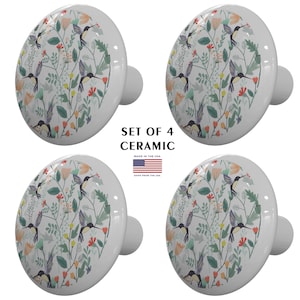 May include: Set of four ceramic cabinet knobs featuring a colorful hummingbird and floral pattern. The knobs are white with a round shape and a small post on the back for attaching to a cabinet door.