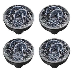 May include: Four black cabinet knobs with a cat design. Each knob features a gray cat illustration on a black and white floral background. The knobs have a round shape with a black base.