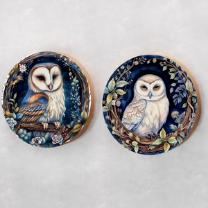 May include: Two round wooden plaques with a dark blue background and gold trim. Each plaque features a detailed illustration of an owl surrounded by foliage and flowers. The owl on the left is a barn owl with brown and white feathers. The owl on the right is a snowy owl with white feathers.