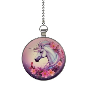 May include: A round, silver-toned ceiling fan pull featuring a unicorn illustration. The unicorn has a white coat, a spiraled horn, and is surrounded by pink flowers. The background is a gradient of pink and purple.