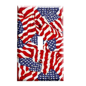 May include: A light switch cover featuring a red, white, and blue American flag pattern. The flags are arranged in a chaotic, overlapping pattern, creating a dynamic and patriotic design.