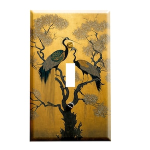 May include: A light switch cover featuring a gold background with a black silhouette of two cranes perched on a tree branch. The cranes are detailed with black, green, and white accents.