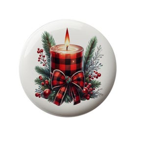 May include: A red and black plaid candle with a lit flame, surrounded by green pine branches and red berries. The candle has a red bow with white polka dots.