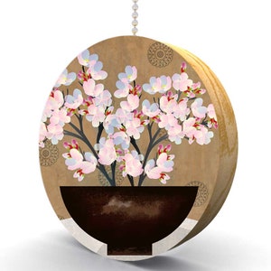 May include: A round wooden pull chain with a brown background and a design of pink and white flowers in a brown pot. The background has a pattern of small circles.