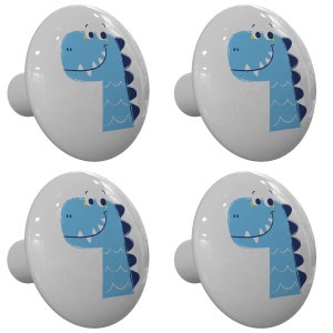 May include: Set of four white ceramic cabinet knobs with a blue dinosaur design. Each knob features a blue dinosaur with a yellow eye and a white smile. The dinosaur is outlined in navy blue and has a wavy pattern on its neck.