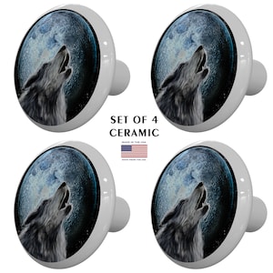 May include: Set of four ceramic cabinet knobs featuring a howling wolf silhouette against a full moon backdrop. The wolf is gray and the moon is blue with a white center. The background is black with white stars.