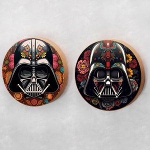 May include: Two round wooden coasters featuring a black and white illustration of Darth Vader's helmet with colorful floral patterns around the helmet. The floral patterns are reminiscent of Mexican Day of the Dead decorations.