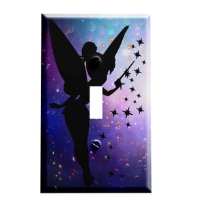 May include: A light switch cover featuring a silhouette of a fairy with wings and a wand, against a purple and blue galaxy background with stars.