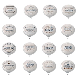 May include: A set of 16 ceramic laundry room signs with various designs and sayings. The signs are oval shaped and have a white background with brown and blue lettering. Some of the sayings include "Laundry Basket", "My Laundry Breeds While I Sleep", "Laundry Room Help Wanted", and "Laundry Co. Open 24 Hours".
