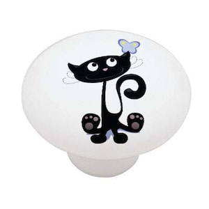 May include: A white ceramic knob with a black cat design. The cat is looking up at a blue butterfly.