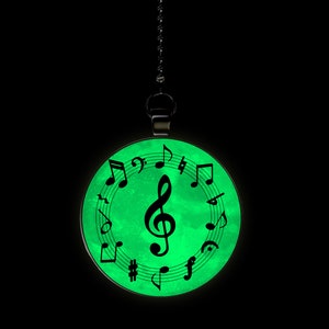 May include: A round, green glow-in-the-dark pendant with a black treble clef and musical notes around the edge. The pendant is attached to a black chain.