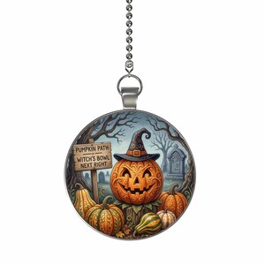 May include: A round ceiling fan pull chain ornament featuring a colorful illustration of a carved jack-o'-lantern wearing a witch hat. A wooden signpost reads PUMPKIN PATH WITCH'S BOWL NEXT RIGHT. The scene includes various pumpkins and a graveyard.