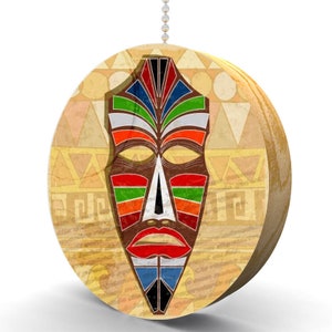 May include: A round, wooden pull chain with a colorful African mask design. The mask has a brown face with yellow eyes, red lips, and a blue and green patterned design.