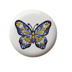 May include: A white ceramic plate with a blue and yellow butterfly design. The butterfly has intricate details and is painted in a traditional style.
