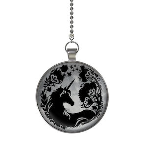 May include: A silver chain with a round pendant featuring a black silhouette of a unicorn surrounded by floral designs on a gray background.