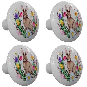May include: Four white ceramic cabinet knobs with a watercolor design of a brown rabbit sitting in a wreath of spring flowers. The flowers are pink, purple, yellow, and white.