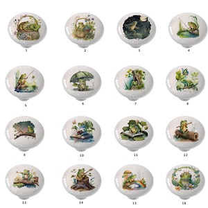 May include: Set of 16 ceramic cabinet knobs featuring whimsical frog illustrations. Each knob depicts a different frog scene, including frogs fishing, reading, playing music, and enjoying nature. The knobs are white with colorful watercolor designs.
