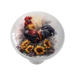 May include: A white ceramic cabinet knob featuring a watercolor painting of a rooster with red, gold, and black feathers. The rooster stands among sunflowers and purple flowers, set against a soft, cloudy background.